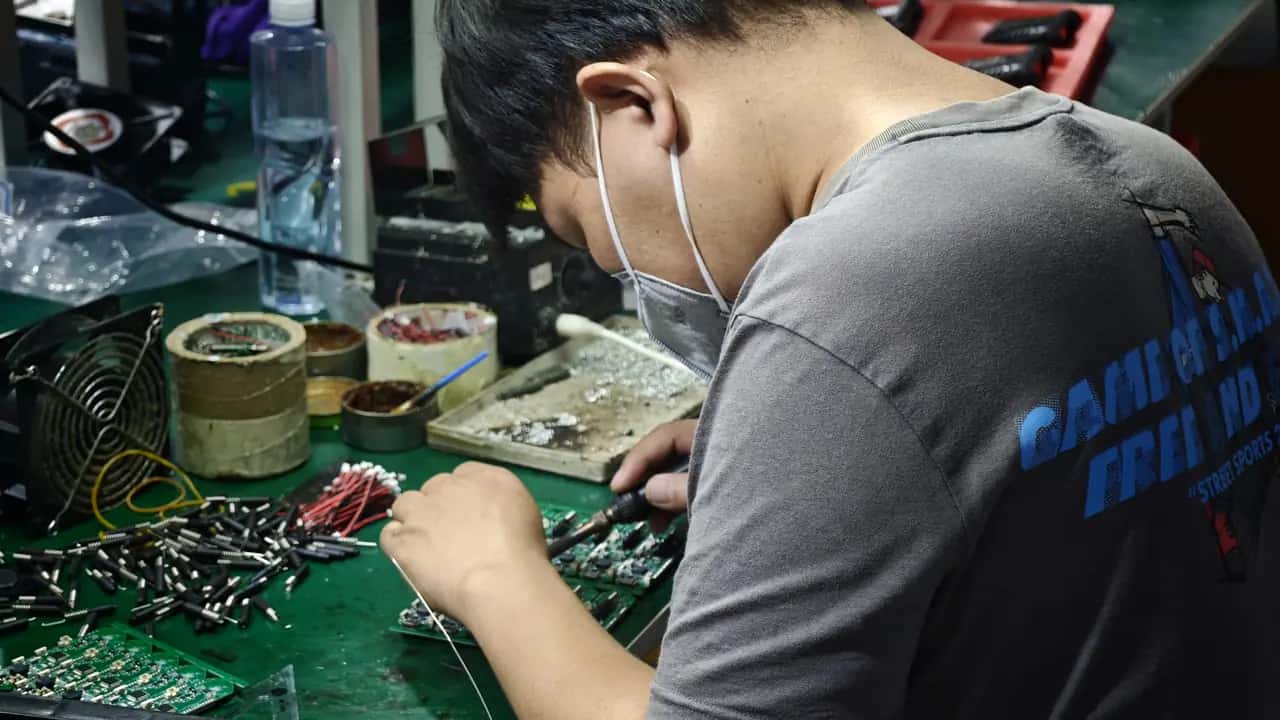 Монтажник паяет плату датчика давления в шинах на сборочной линии TPMS